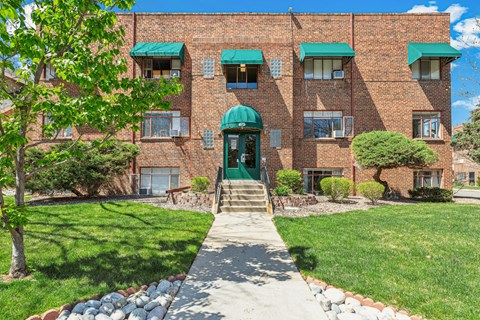 A brick building with a green awning and a stone pathway leading to the front door.