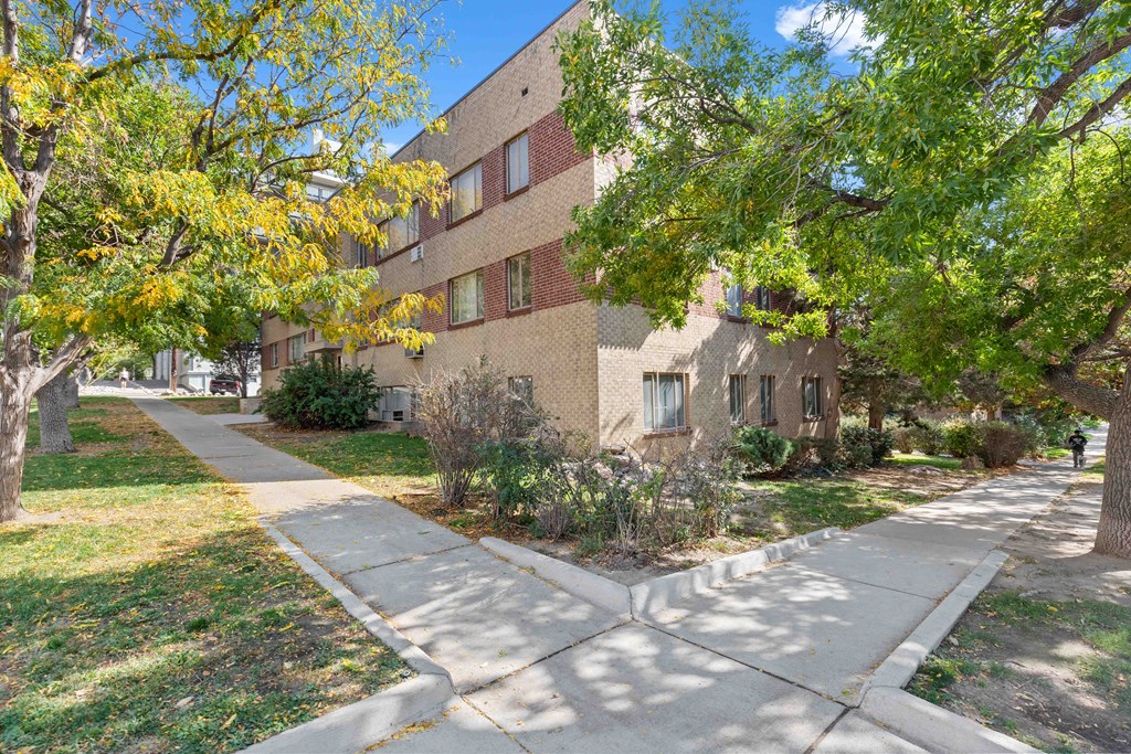 an apartment building with a sidewalk and trees in front of it