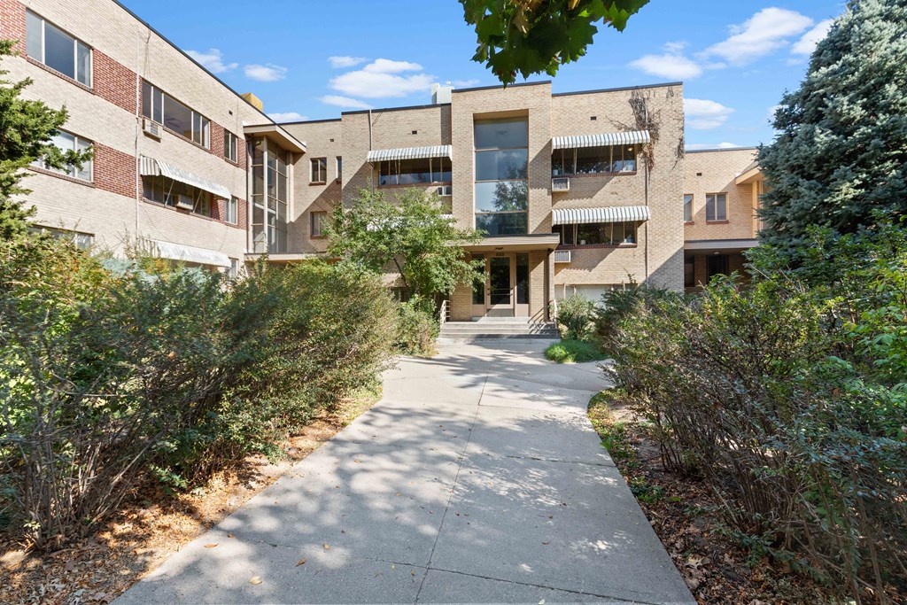 a sidewalk in front of a building with trees and bushes