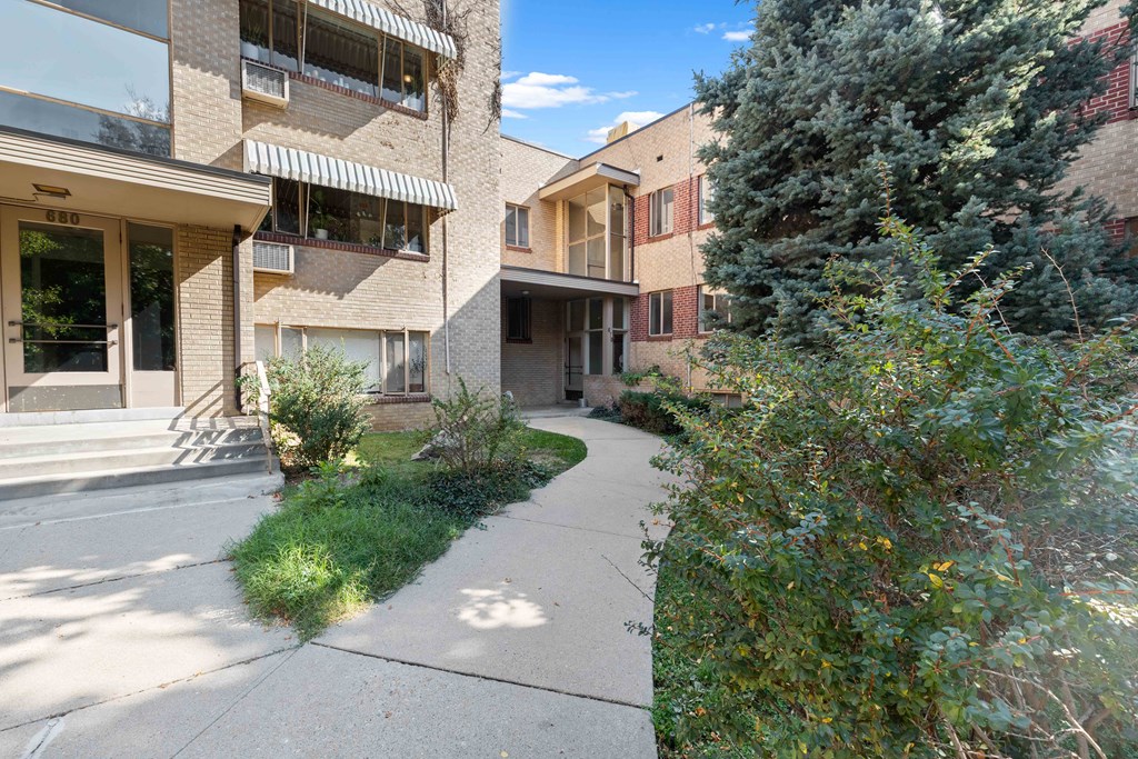 a sidewalk in front of a building with trees and bushes