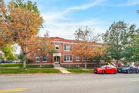 A red car is parked on the street in front of a brick building.