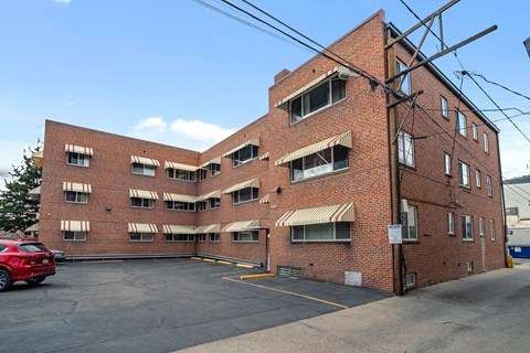 A red car is parked in a parking lot in front of a brick building.
