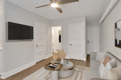 A living room with a white couch, a coffee table, and a flat screen TV mounted on the wall.