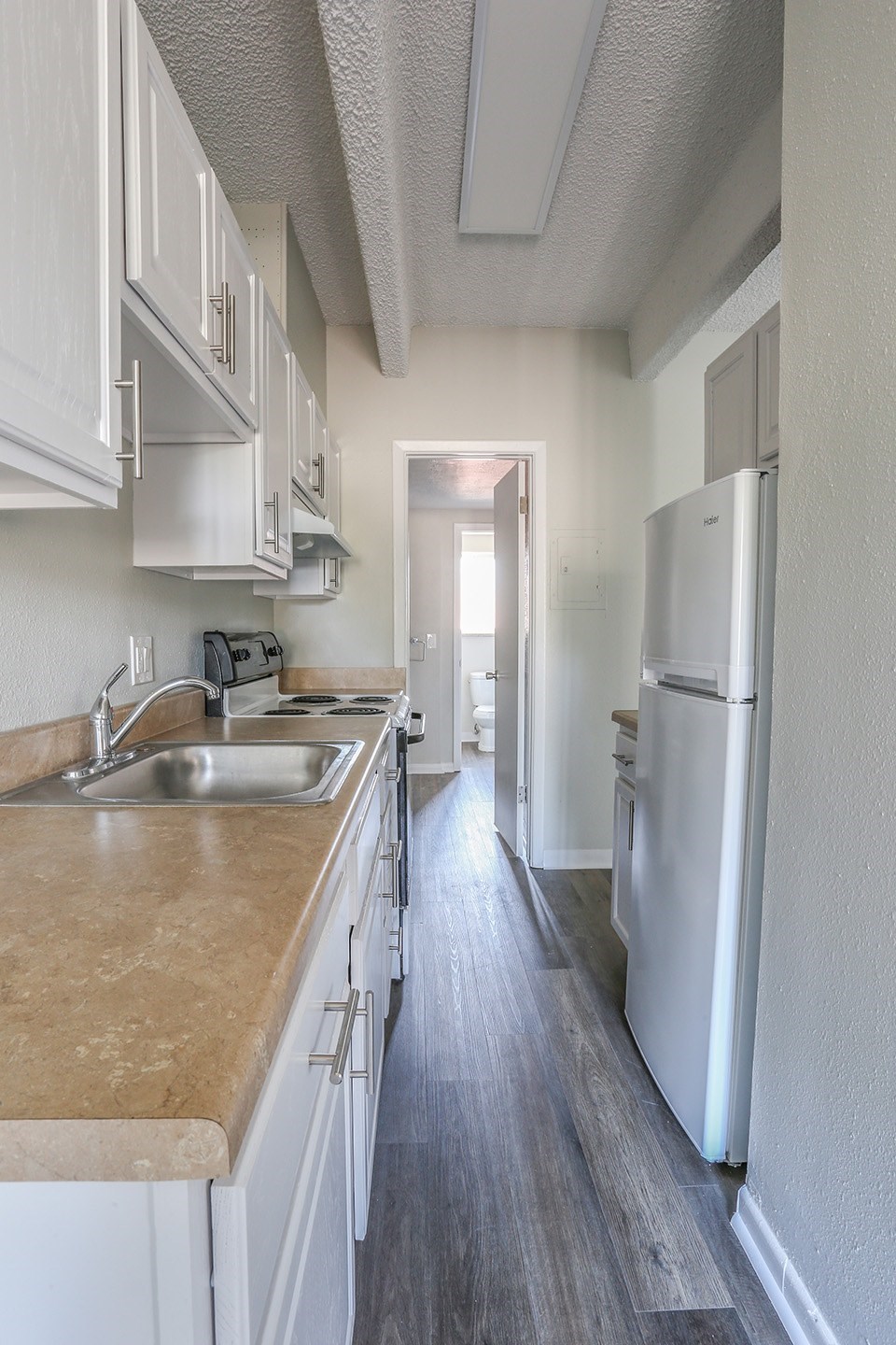 A long, narrow kitchen with white cabinets and a white refrigerator.