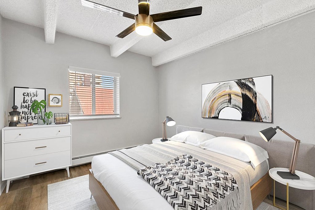 A bedroom with a bed, a ceiling fan, and a painting on the wall.