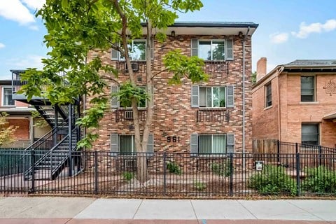 A brick building with a black fence and a tree in front.