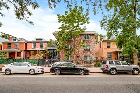 Three cars are parked in front of a row of houses.