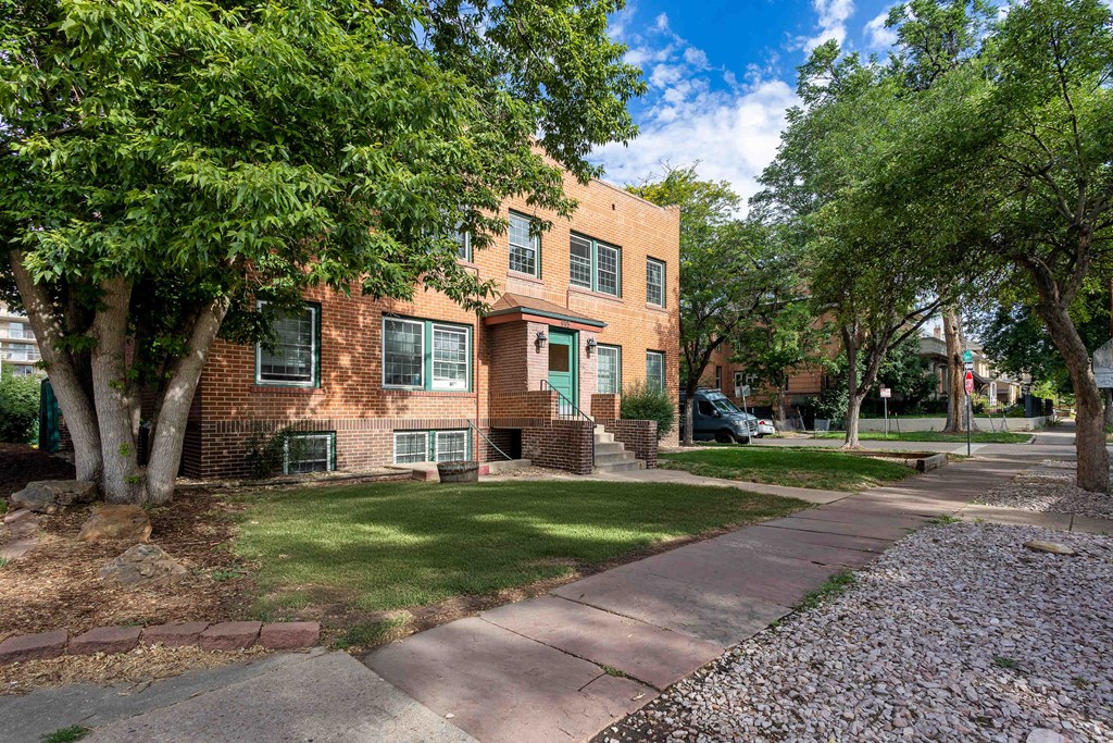 a brick apartment building with green trees and a sidewalk