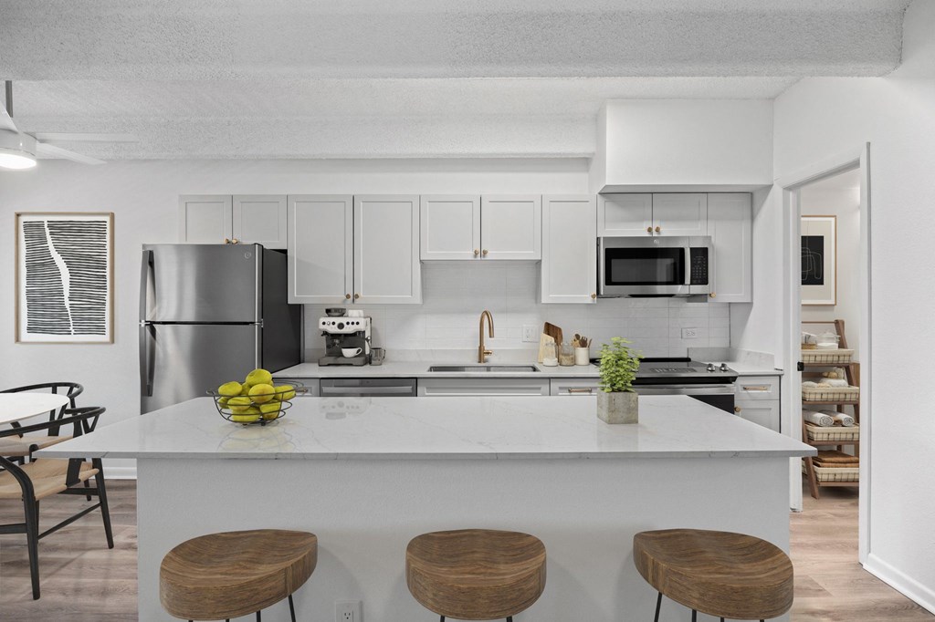 A kitchen with white cabinets and a white island with three stools.
