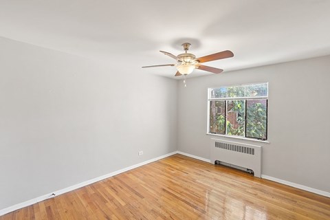 A room with a ceiling fan and a window with a view of a garden.
