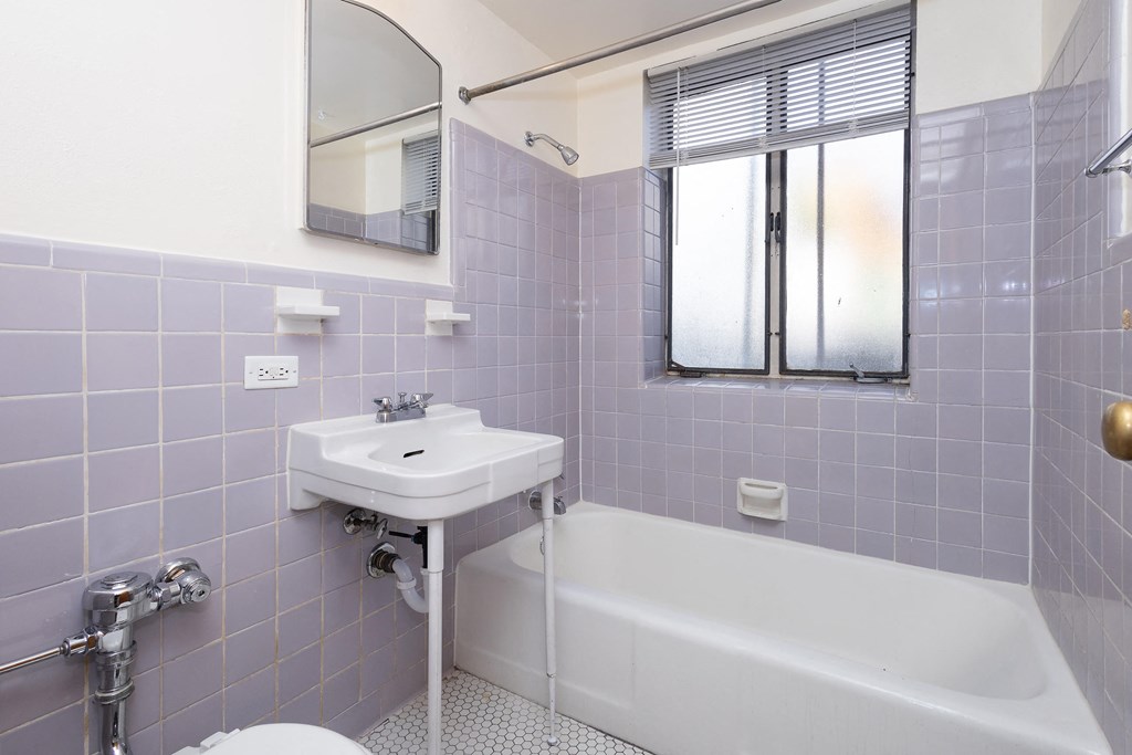 A white sink is on a purple tiled wall next to a white bathtub.