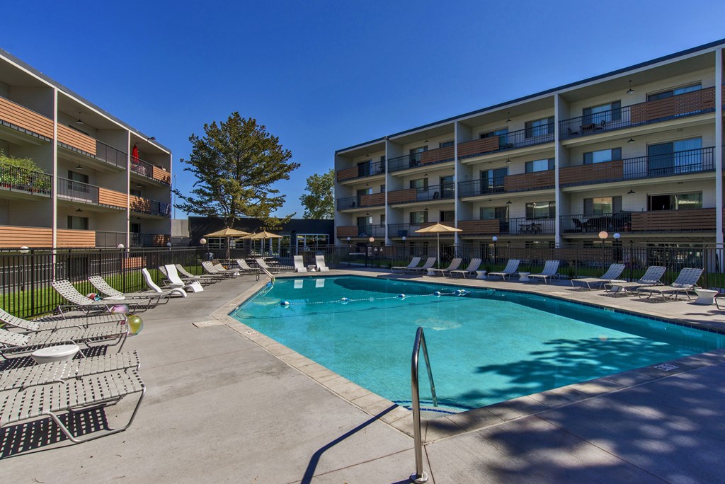 A swimming pool surrounded by lounge chairs and apartment buildings.