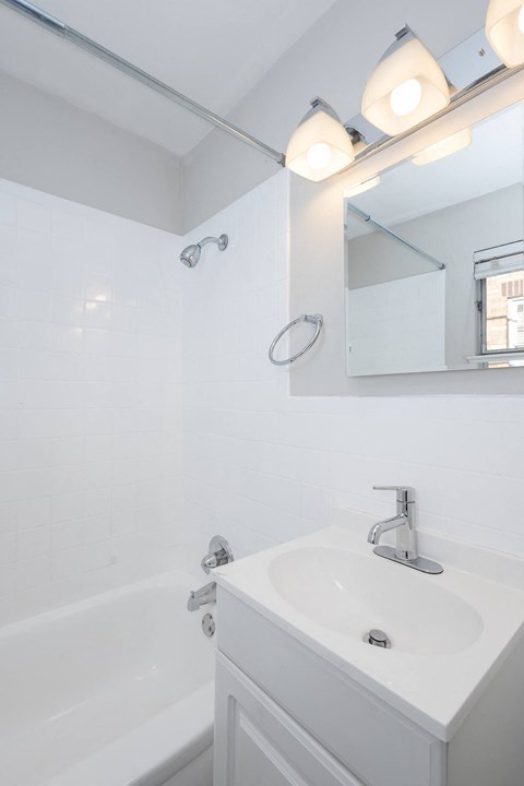 A white bathroom with a sink, mirror, and lighting fixture.