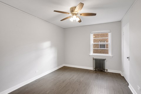 A room with a ceiling fan and a window with a radiator beneath it.