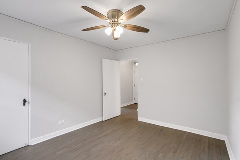 A room with a ceiling fan and light fixture, two doors, and a wooden floor.
