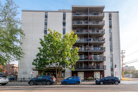 A tall apartment building with cars parked in front.