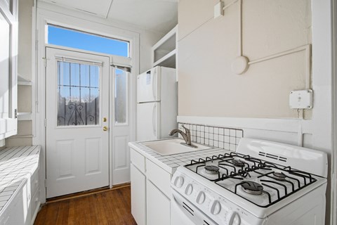 A white kitchen with a gas stove and a window.