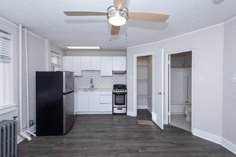 A black refrigerator sits in a kitchen with white walls and a ceiling fan.