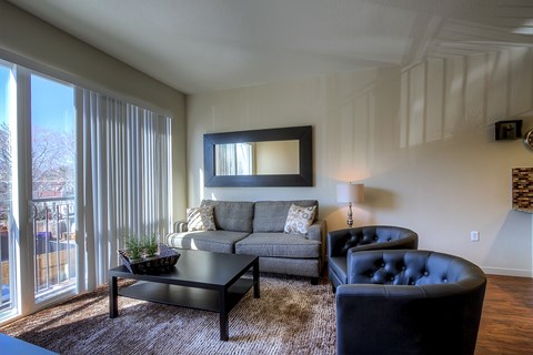 A living room with a grey couch, a black leather chair, and a large mirror on the wall.