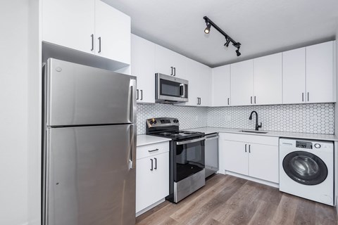 A modern kitchen with a refrigerator, microwave, oven, and washing machine.