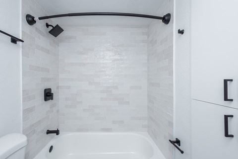A white tiled bathroom with a black shower head and faucet.