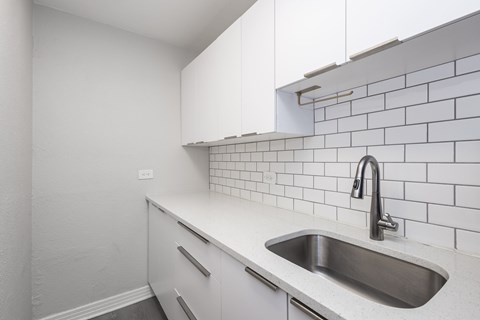 A kitchen with a white sink and white cabinets.