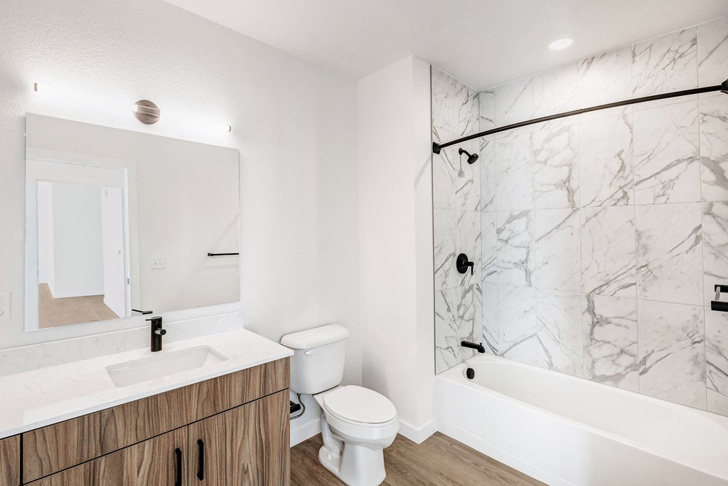 A white bathroom with a marble wall and a wooden vanity.