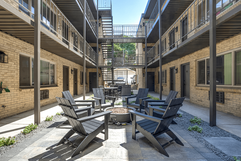 A courtyard with black chairs and tables surrounded by brick buildings.