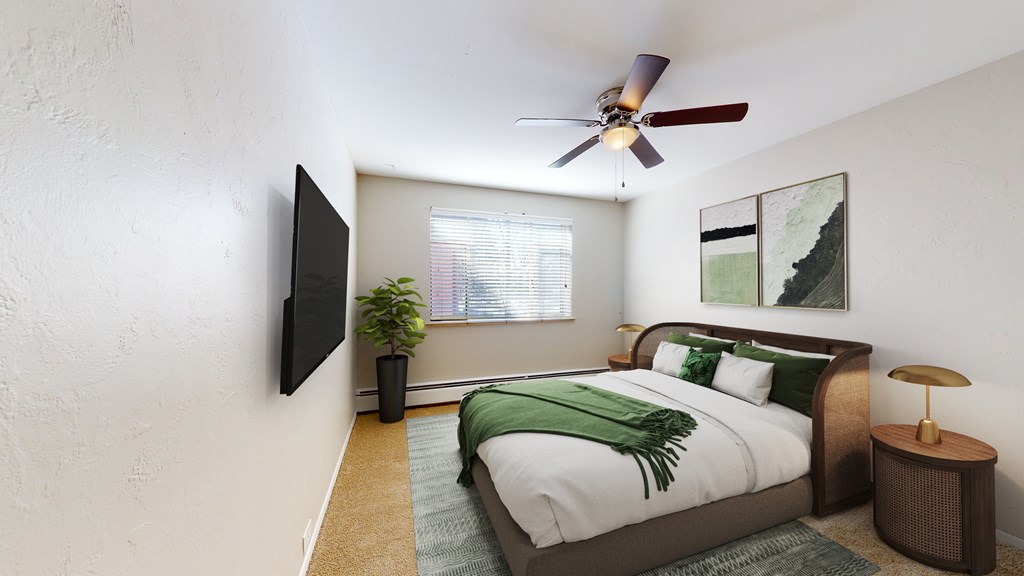 A bedroom with a bed, a plant, a television, and a ceiling fan.