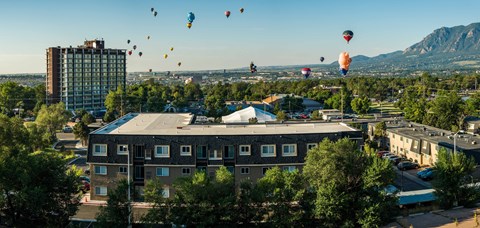 a group of hot air balloons flying over a city with a tall building and buildings