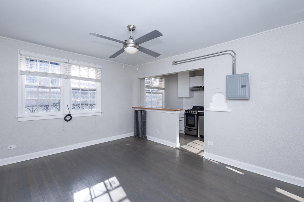 A room with a ceiling fan and a kitchen area in the background.
