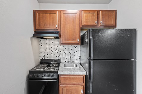 A kitchen with a black refrigerator, black stove, and wooden cabinets.
