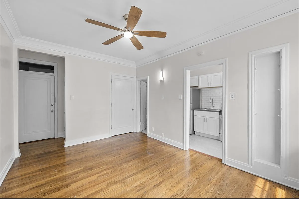 an empty living room with a ceiling fan and a kitchen