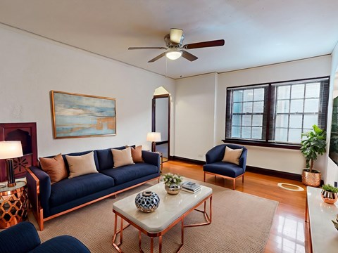 A living room with a blue couch, a painting on the wall, and a ceiling fan.
