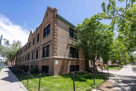 A red brick building with a green roof and a tree in front.