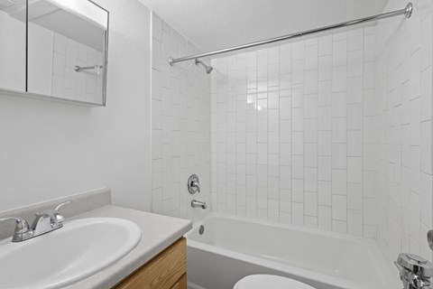 A white tiled bathroom with a white sink and bathtub.