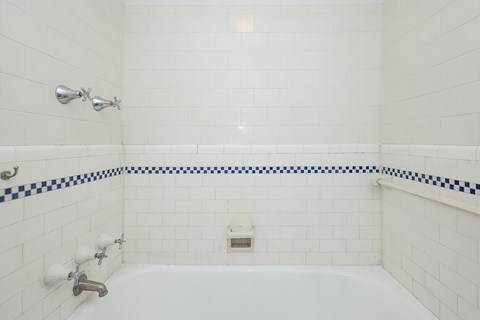 A white tiled bathroom with a blue and white border on the edge of the tub.