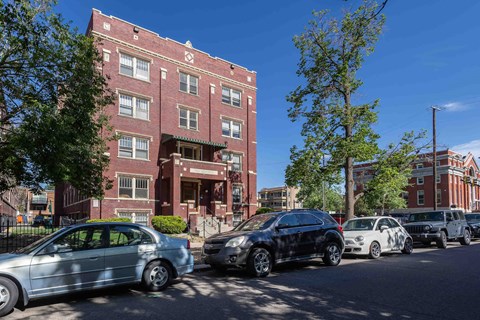 A row of cars parked on a street in front of a red brick building.