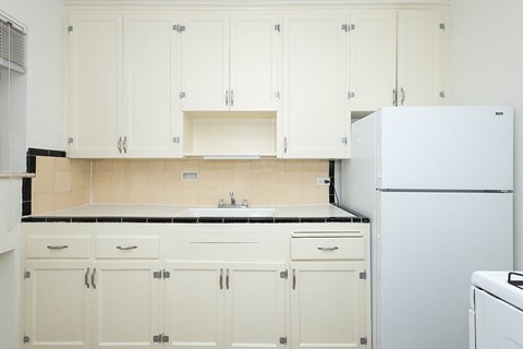 A white kitchen with a refrigerator on the right.
