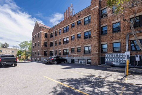 A parking lot in front of a brick building with a truck and a car parked.