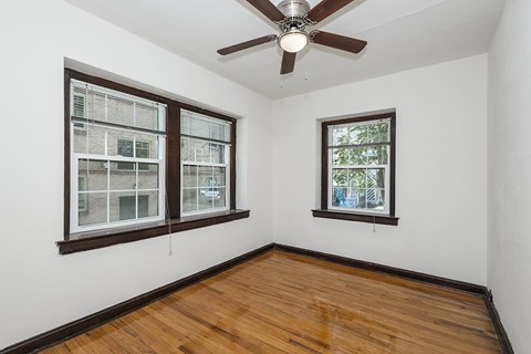 A room with a ceiling fan and two windows.