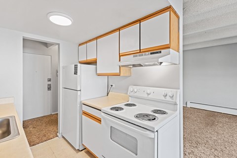 A white kitchen with wooden cabinets and a stove top oven.