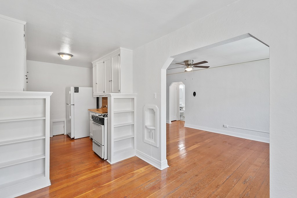 A white kitchen with wooden floors and a ceiling fan.