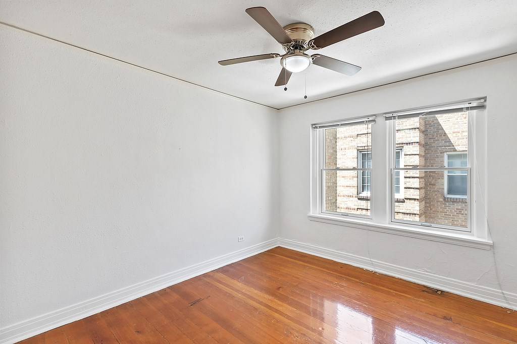 A room with a ceiling fan and a window showing a view of a building outside.
