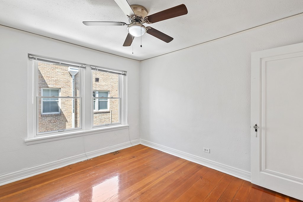 A room with a ceiling fan and two windows.