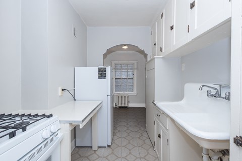 A white kitchen with a stove, sink, and cabinets.