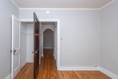 A room with a wooden floor and a white wall with a doorway leading to another room.