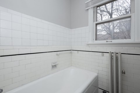 A white tiled bathroom with a tub and a window.