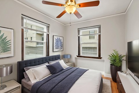 A bedroom with a bed, a ceiling fan, and a window with blinds.