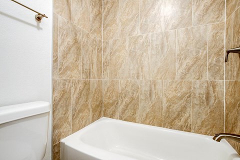 A white bathtub sits next to a white toilet in a bathroom.